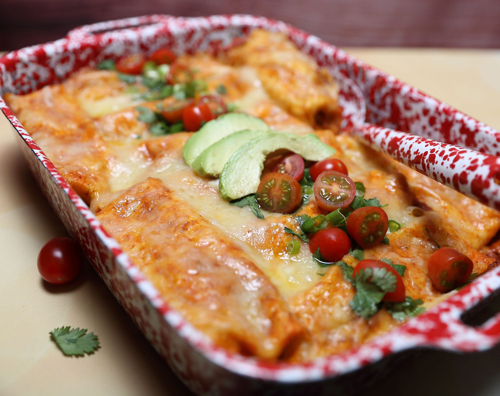 Top view of sausage enchiladas in a red and white pan garnished with avocado and tomato